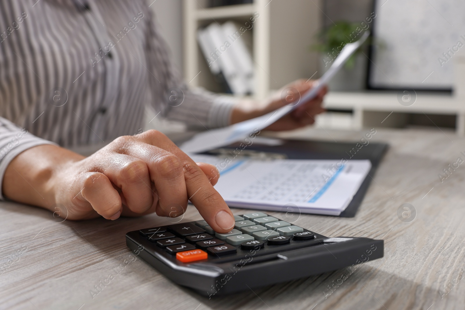 Photo of Woman using calculator at light wooden table in office, closeup