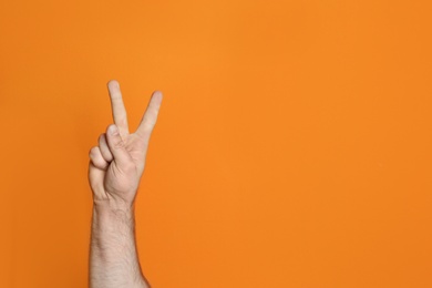 Photo of Young man showing victory gesture on color background. Space for text