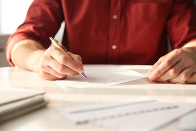 Man writing letter at white table in room, closeup