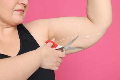 Photo of Obese woman with scissors on pink background, closeup. Weight loss surgery