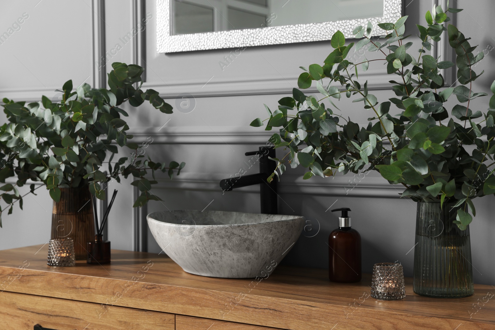 Photo of Eucalyptus branches, aroma sticks and candles near vessel sink on bathroom vanity. Interior design