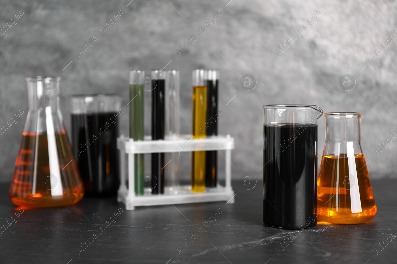 Photo of Beakers, flasks and test tubes with different types of oil on grey textured table, closeup