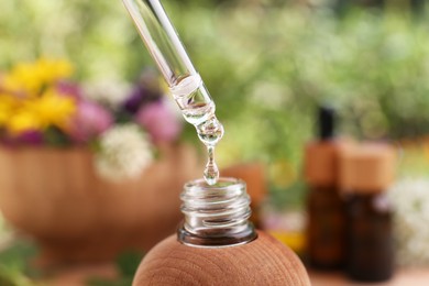 Dripping essential oil from pipette into bottle on blurred background, closeup