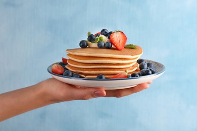 Photo of Woman holding delicious pancakes with fresh berries and butter against light blue background, closeup