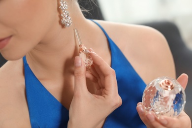Young woman applying perfume on neck indoors, closeup