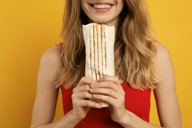 Young woman with delicious shawarma on yellow background, closeup