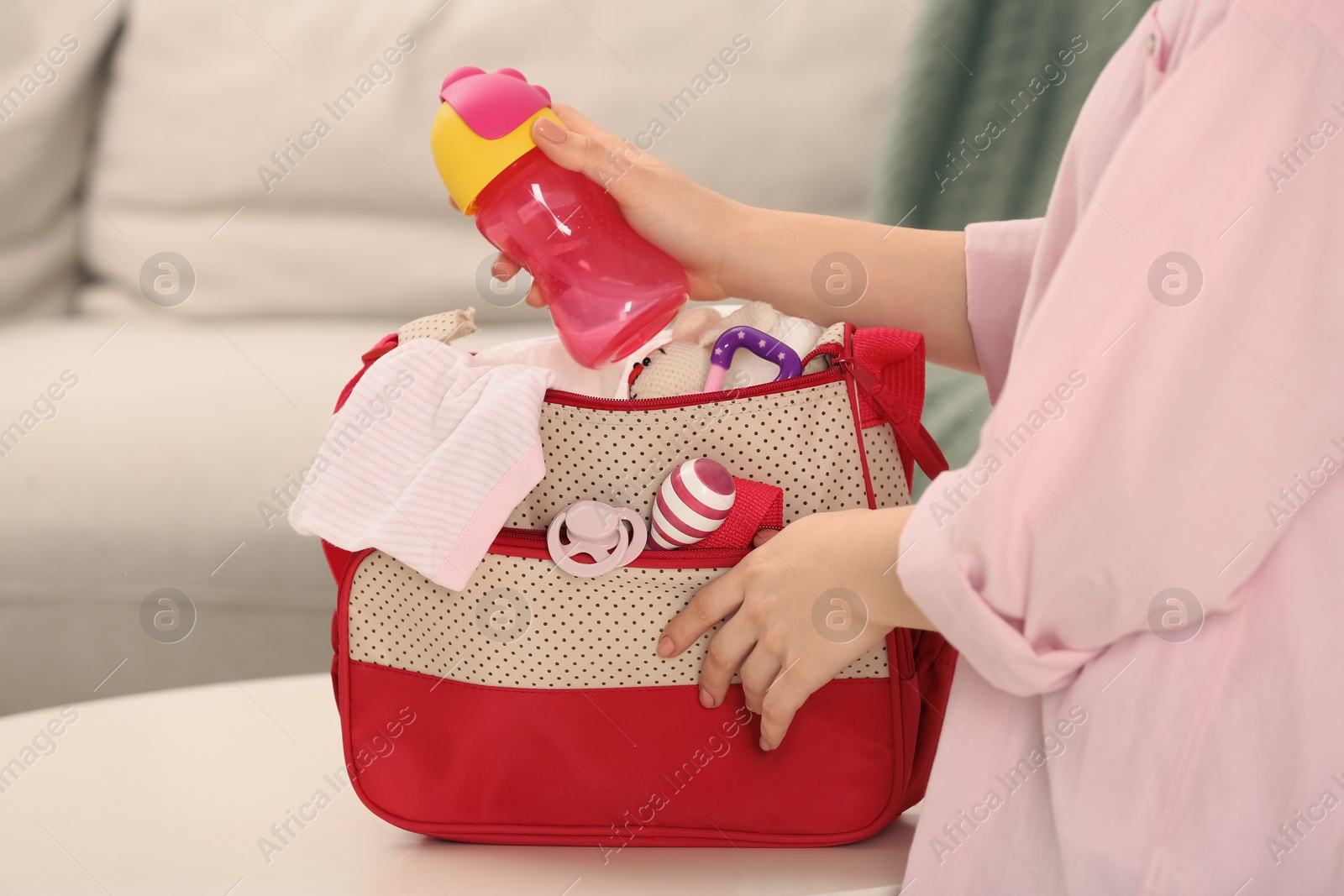 Photo of Woman putting baby`s bottle into mother`s bag at white table indoors, closeup