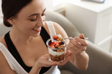 Photo of Woman eating tasty granola with fresh berries and yogurt at home