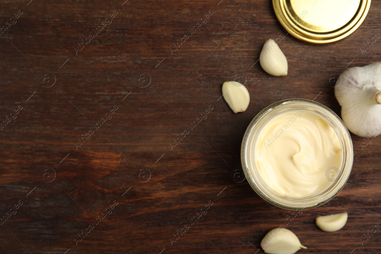 Photo of Jar of delicious mayonnaise and fresh garlic on wooden table, flat lay. Space for text