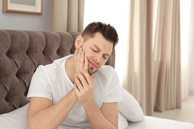 Man suffering from tooth pain in bedroom