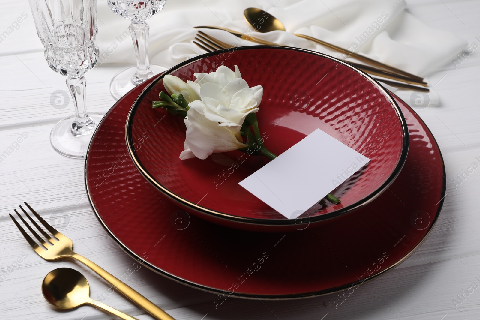 Photo of Stylish table setting. Dishes, cutlery, blank card and flower on white wooden background, closeup