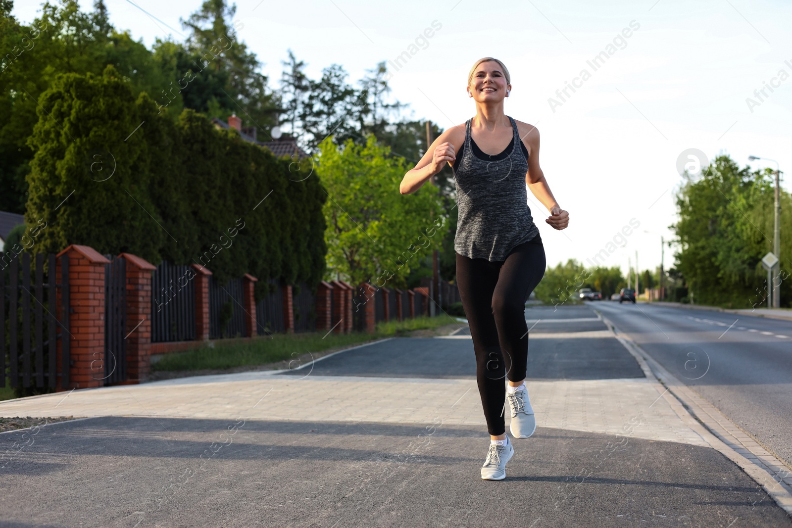 Photo of Woman with wireless earphones jogging around neighborhood in morning