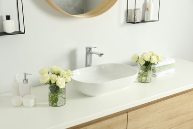 Photo of White sink between beautiful roses and toiletries in bathroom