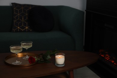 Burning candle, glasses of wine and beautiful red rose on wooden table in room