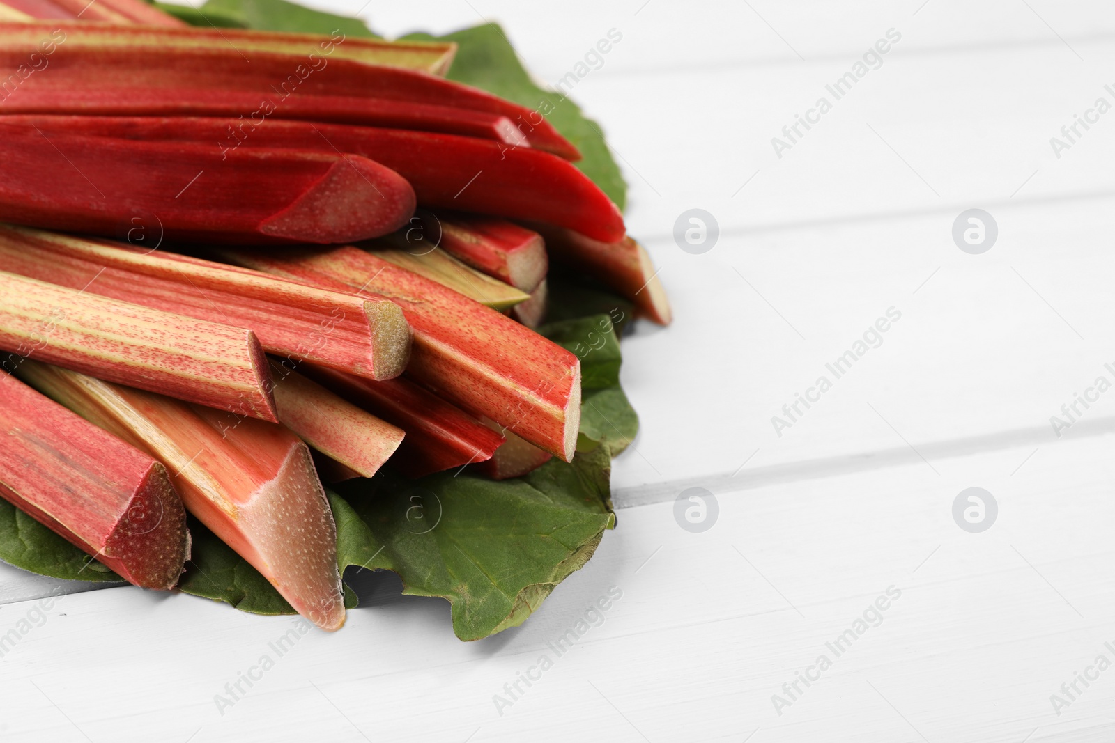 Photo of Many cut rhubarb stalks and leaf on white wooden table, closeup. Space for text