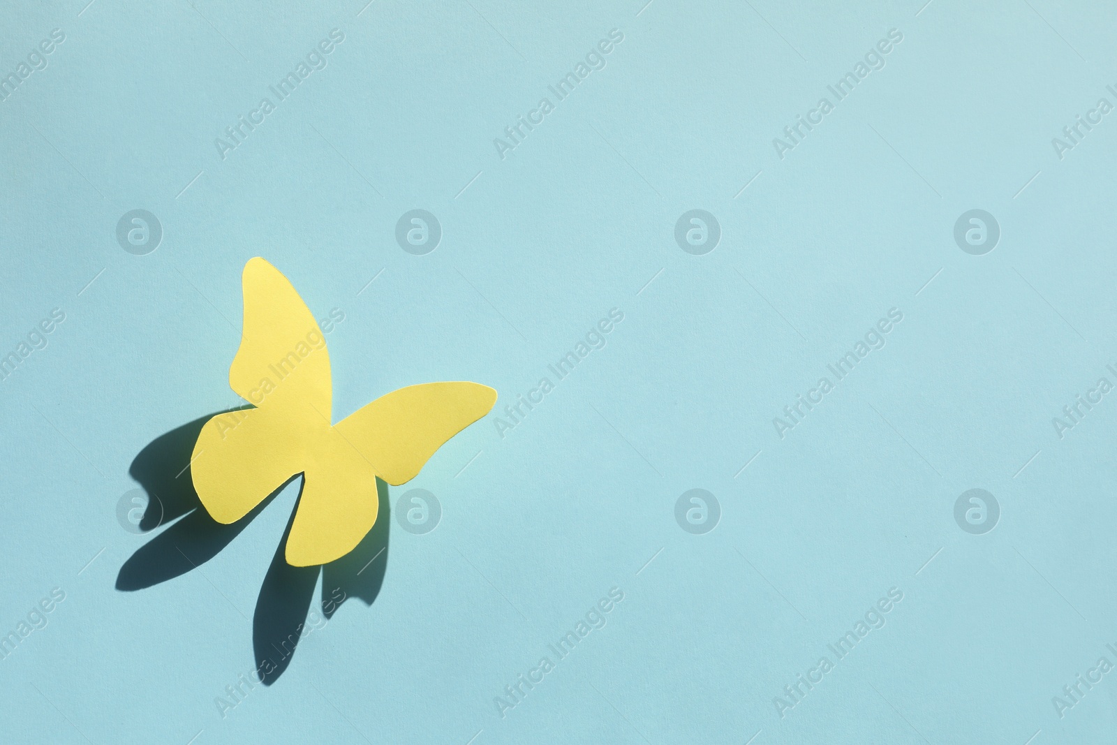 Photo of Yellow paper butterfly on turquoise background, top view. Space for text