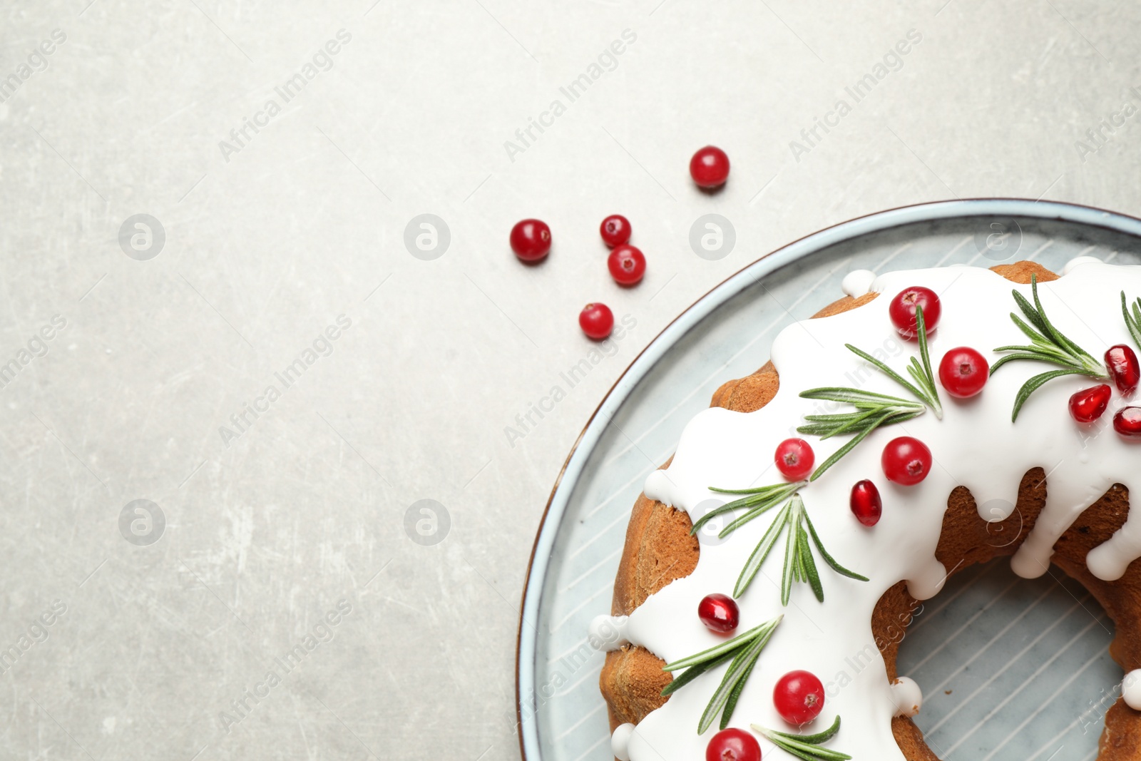 Photo of Traditional Christmas cake decorated with glaze, pomegranate seeds, cranberries and rosemary on light grey table, flat lay. Space for text