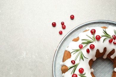 Photo of Traditional Christmas cake decorated with glaze, pomegranate seeds, cranberries and rosemary on light grey table, flat lay. Space for text