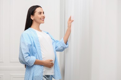 Photo of Happy pregnant woman near window indoors, space for text