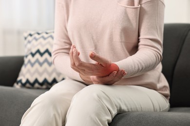 Woman suffering from pain in wrist on sofa, closeup