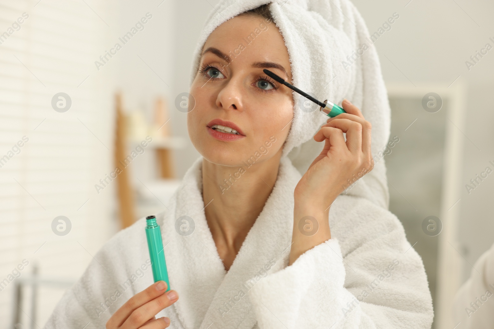 Photo of Beautiful woman applying mascara with brush indoors