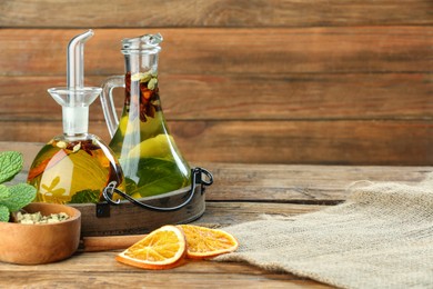 Photo of Cooking oil with different spices and herbs in jugs on wooden table. Space for text