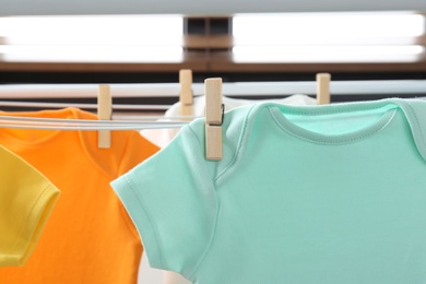 Photo of Different cute baby onesies hanging on clothes line indoors. Laundry day