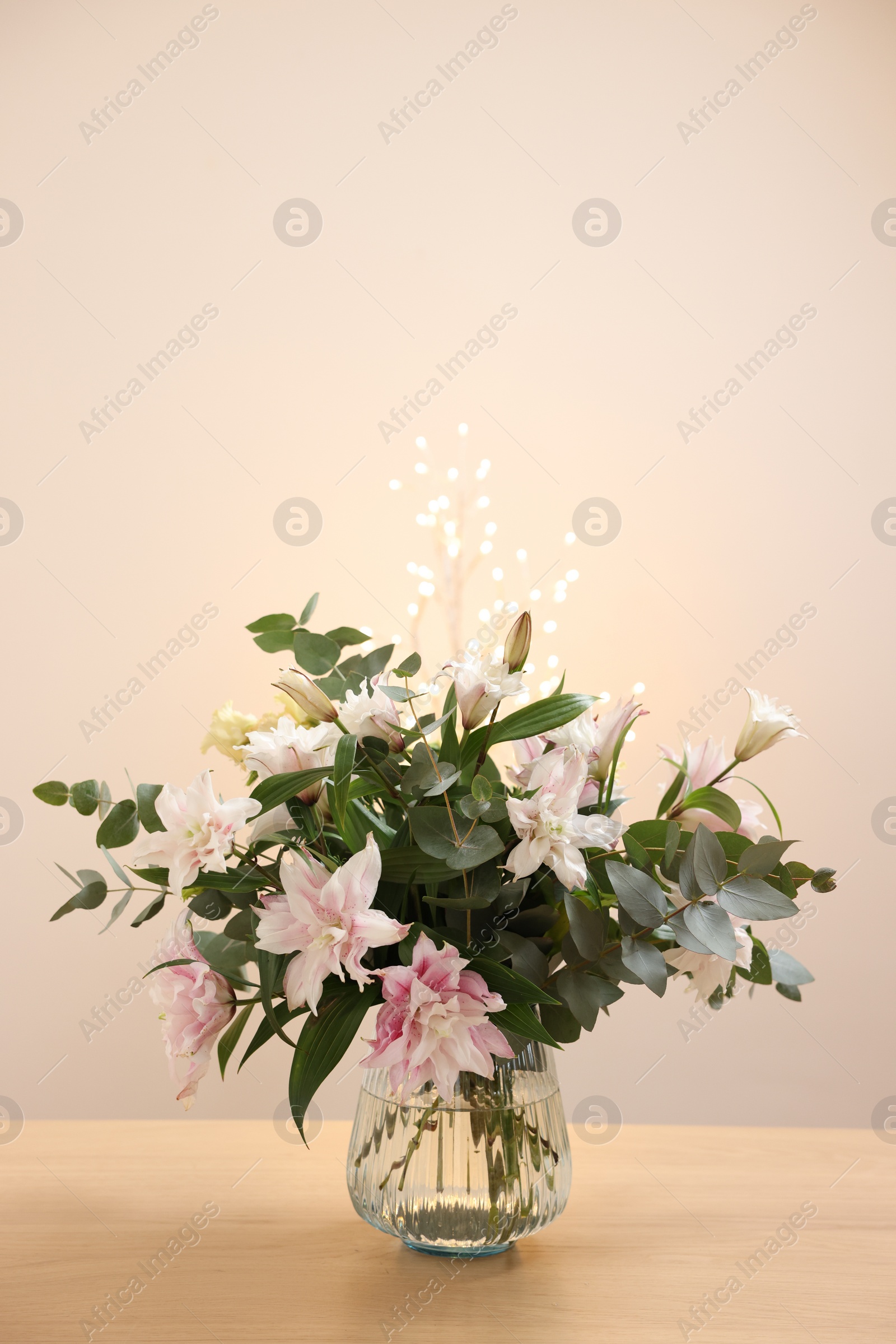 Photo of Bouquet of beautiful lily flowers in vase on wooden table against beige background