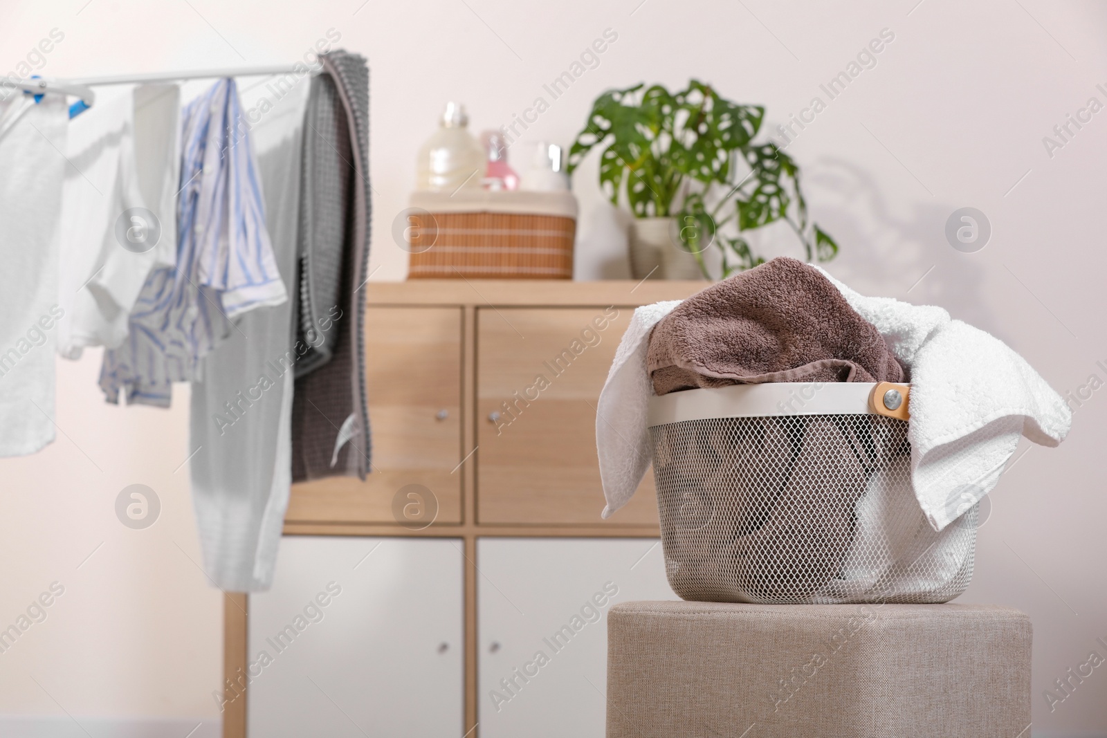 Photo of Plastic laundry basket with clothes on stylish pouf indoors. Space for text