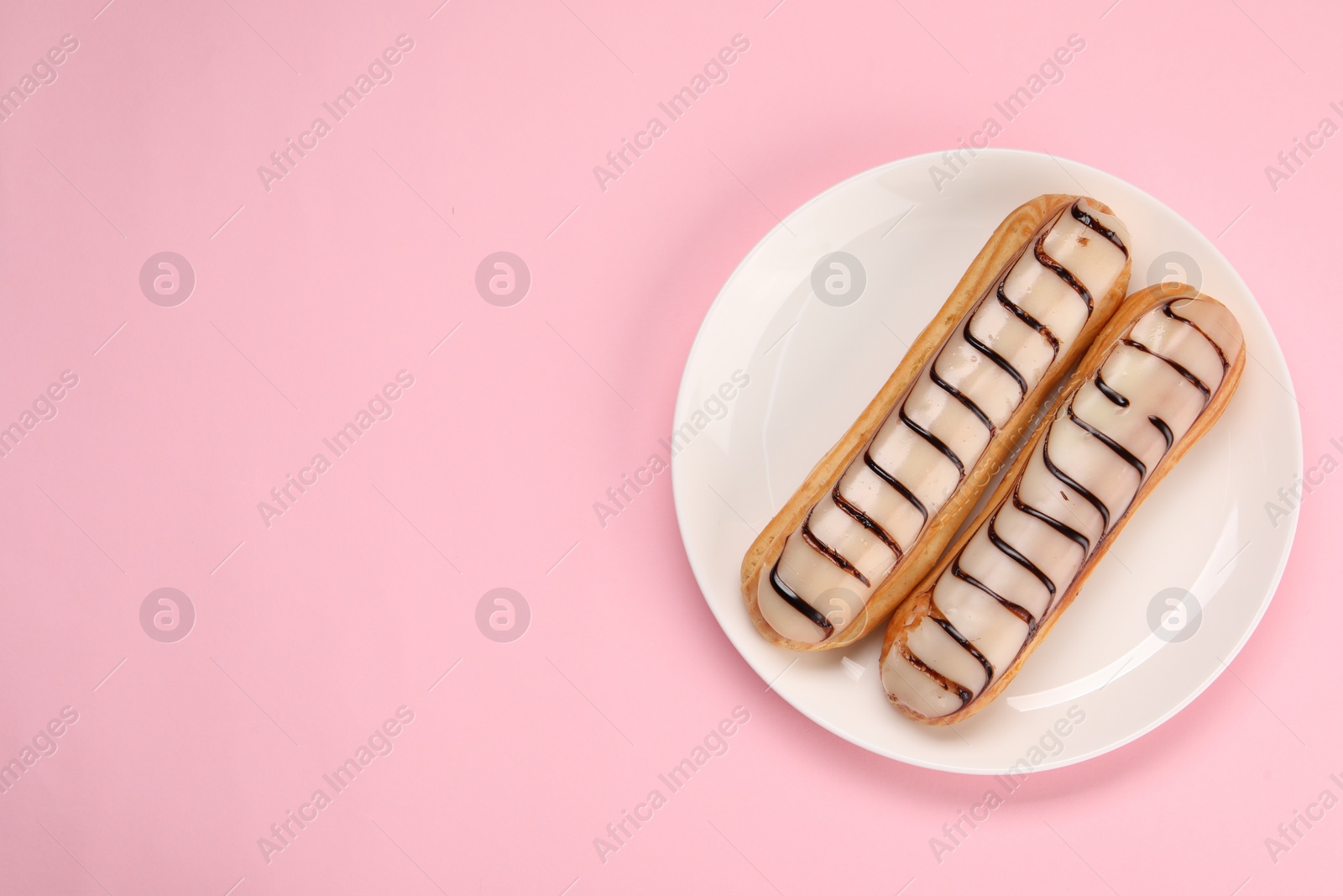 Photo of Delicious eclairs covered with glaze on pink background, top view. Space for text