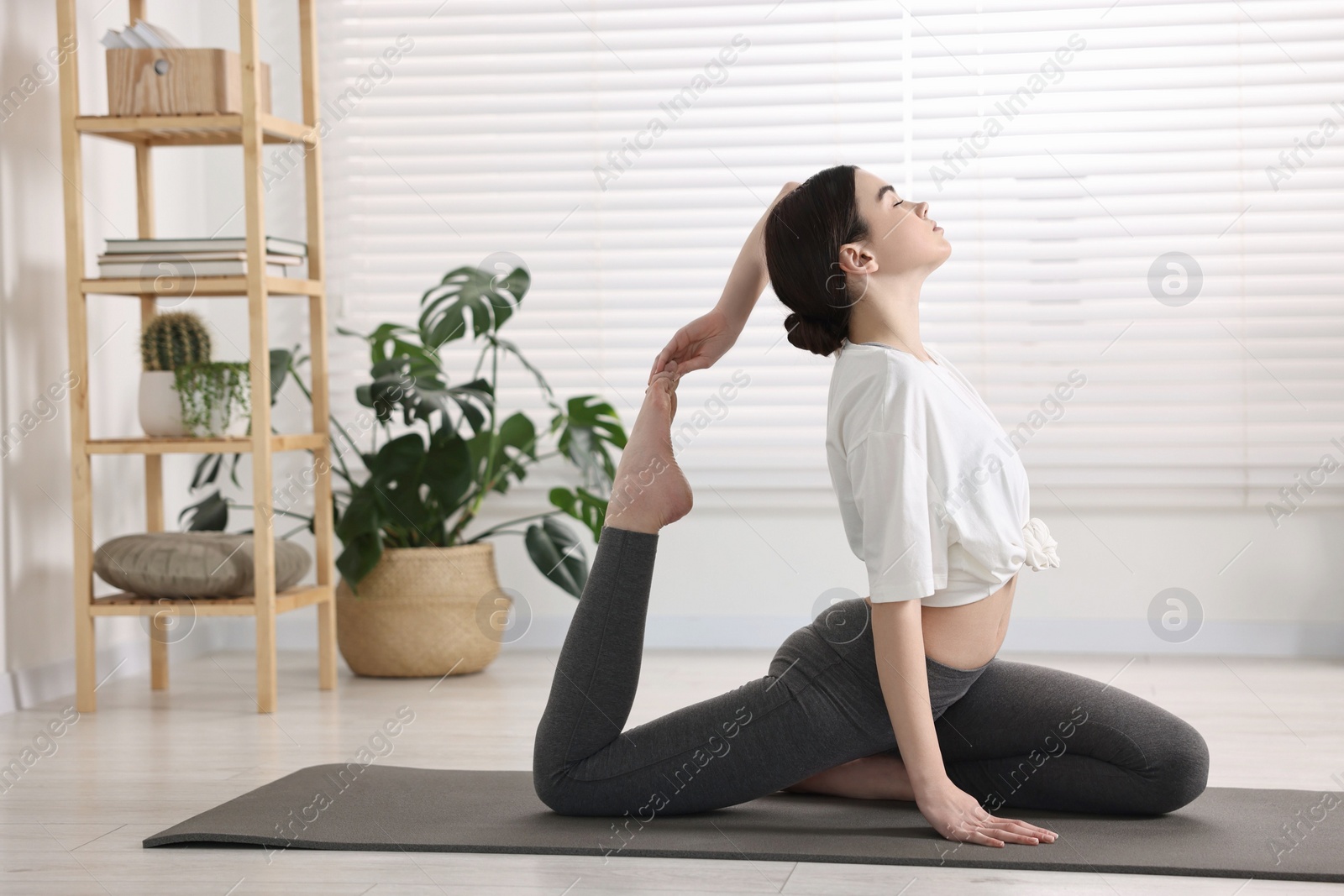 Photo of GIrl practicing one legged king pigeon asana on mat in yoga studio. Eka pada rajakapotasana pose