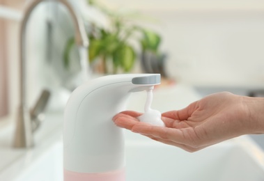 Woman using automatic soap dispenser in kitchen, closeup