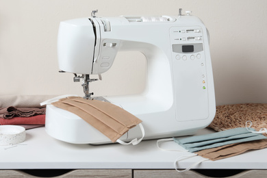 Photo of Sewing machine and homemade protective masks on white table