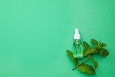 Bottle of essential oil and mint on green background, flat lay. Space for text