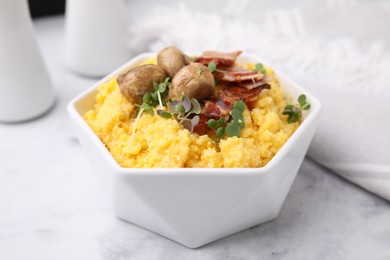 Photo of Cooked cornmeal with bacon, mushrooms and microgreens in bowl on white marble table, closeup