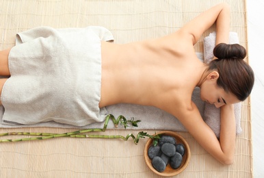 Beautiful young woman relaxing after massage on bamboo mat, top view