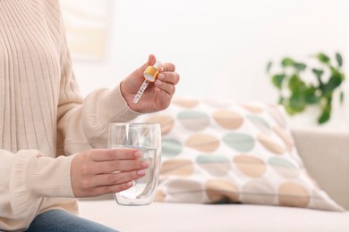 Photo of Woman dripping food supplement into glass of water indoors, closeup. Space for text