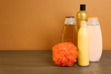 Photo of Different shower gel bottles with pouf on wooden table. Space for text