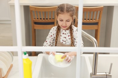 Photo of Little girl washing plate above sink indoors, view from outside