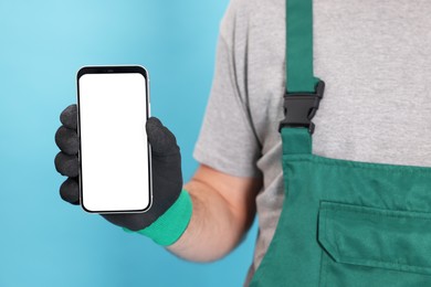 Photo of Professional repairman in uniform with phone on light blue background, closeup