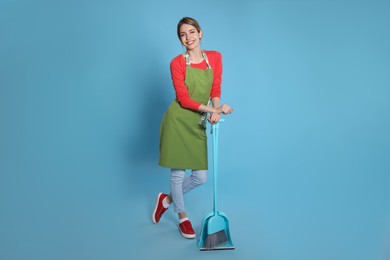 Photo of Young housewife with broom and dustpan on light blue background