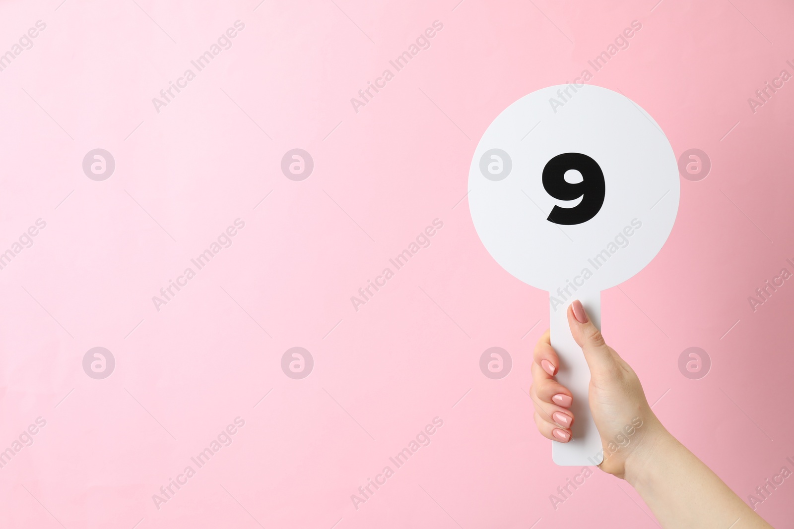 Photo of Woman holding auction paddle with number 9 on pink background, closeup. Space for text