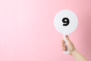 Woman holding auction paddle with number 9 on pink background, closeup. Space for text