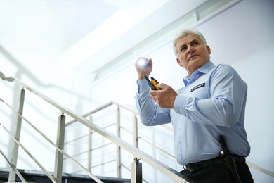 Photo of Professional security guard with portable radio set and flashlight on stairs indoors