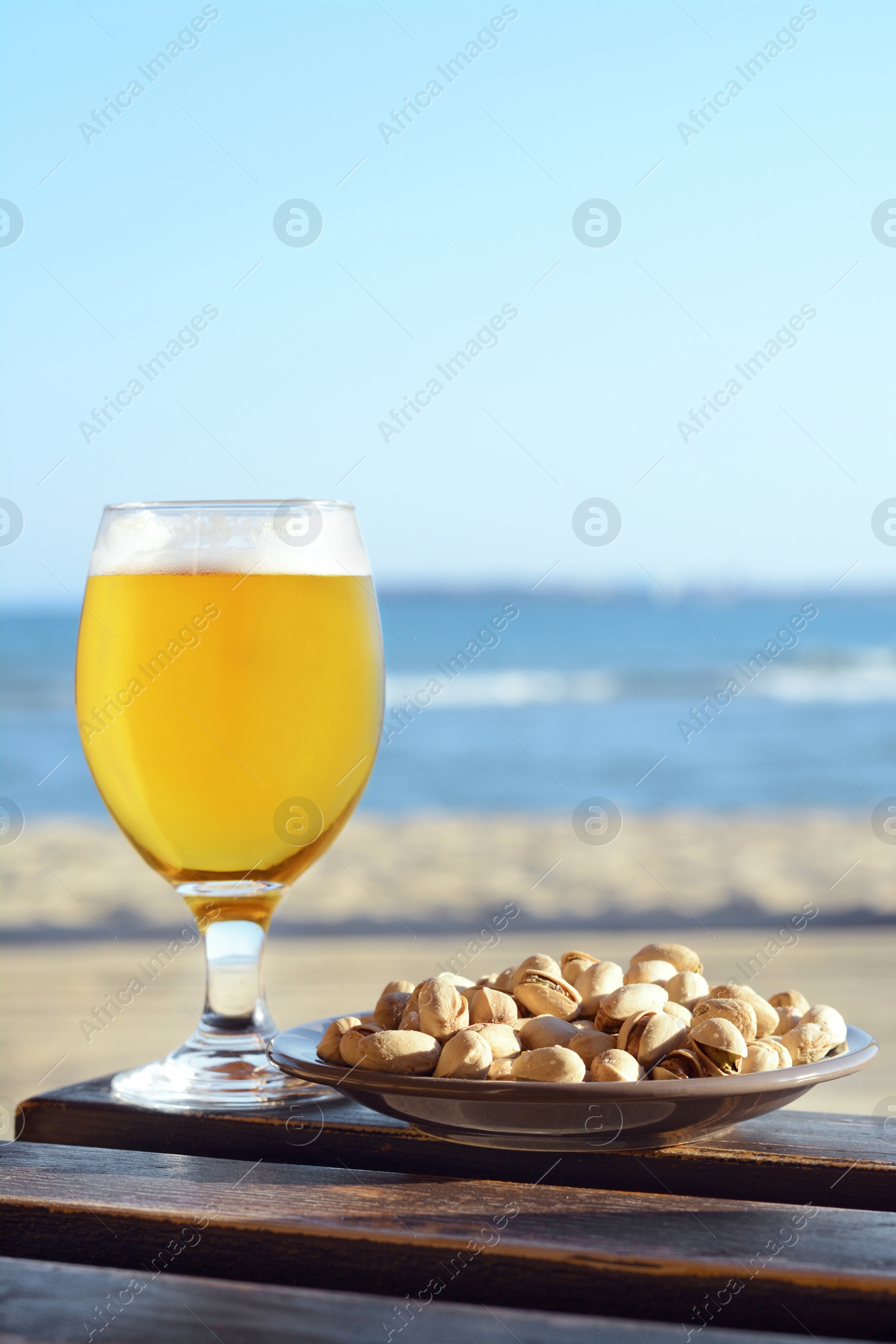 Photo of Glass of cold beer and pistachios on wooden table near sea
