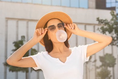 Beautiful woman in stylish sunglasses blowing gum outdoors on sunny day