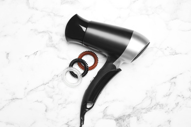 Photo of Hair dryer and spiral rubber bands on white marble table, flat lay