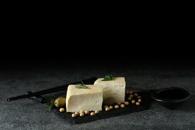 Photo of Pieces of delicious tofu with herbs, olives and soy on grey table, space for text