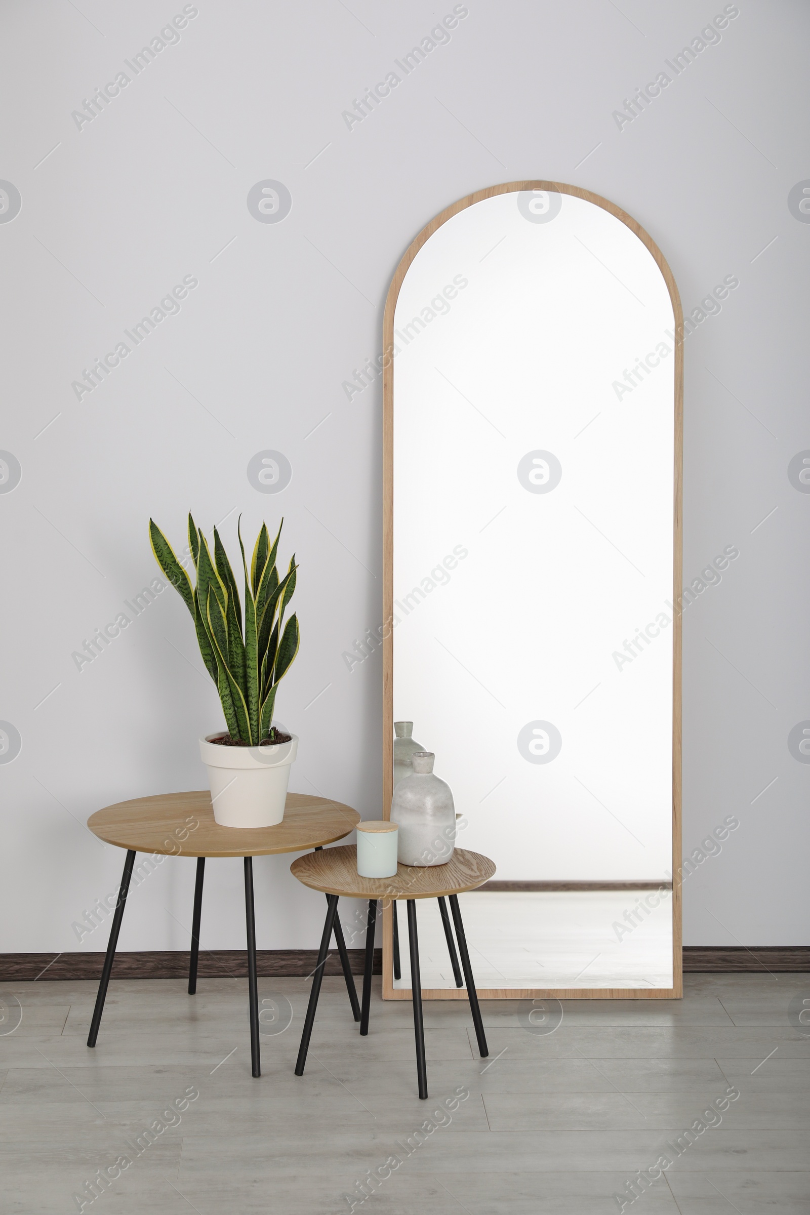 Photo of Leaning floor mirror near nesting tables with houseplant and decor in room