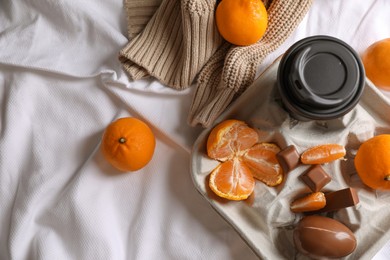 Photo of Delicious ripe tangerines, cup with drink and chocolates on white bedsheet, flat lay